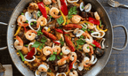 Plato de paella mixta tradicional con mariscos frescos y carnes seleccionadas, lista para servir en casa, porciones para grupos.