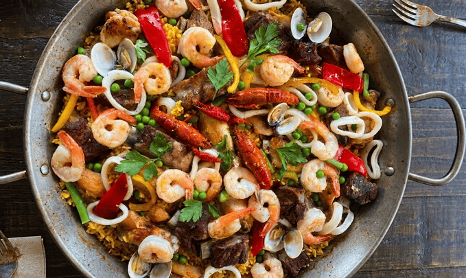 Plato de paella mixta tradicional con mariscos frescos y carnes seleccionadas, lista para servir en casa, porciones para grupos.